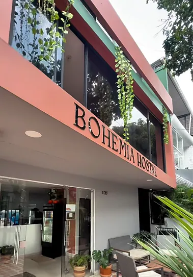 Bohemia’s coral-and-green facade with “BOHEMIA HOSTAL” in black letters, hanging plants over the balcony and a glass entrance with potted plants below.