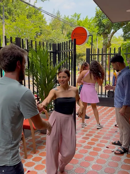 Guests dancing salsa on the orange-and-cream tiled patio at Bohemia’s entrance, a woman in pink trousers mid-turn, the round orange Canela Café sign on the gate behind them.